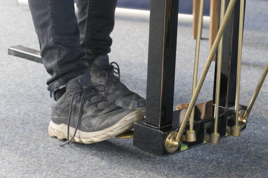 Detailaufnahme von zwei Füßen in Turnschuhen, die das Pedal eines Flügels drücken