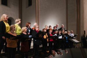 Ein bunt gekleideter Chor mit vielen Frauen und weniger Männern sind auf den Altarstufen der Kulturkirche St. Stephani
