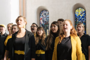 Schwarz-gelb gekleidete Menschen stehen dicht neben- und hintereinander und singen
