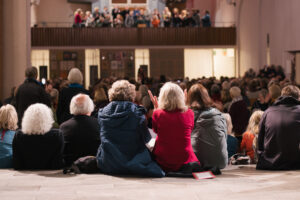 Viele Menschen sitzen in der Kulturkirche St. Stephani, man sieht ihre Rücken, sie schauen zur Empore, auf der ein Chor singt