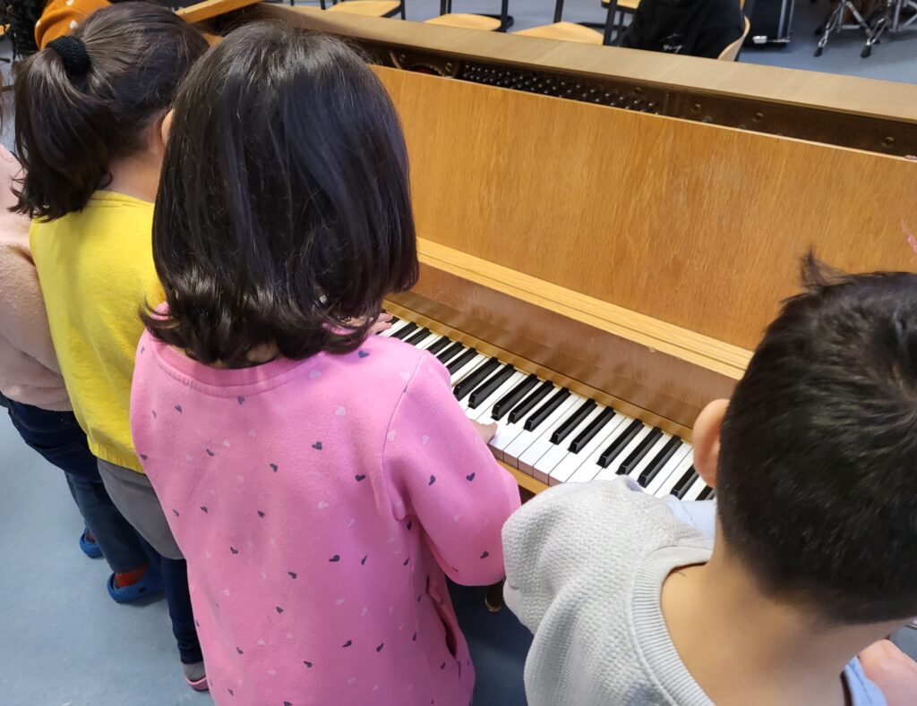 Kinder stehen an einem Klavier und probieren ihre ersten Töne am Instrument aus