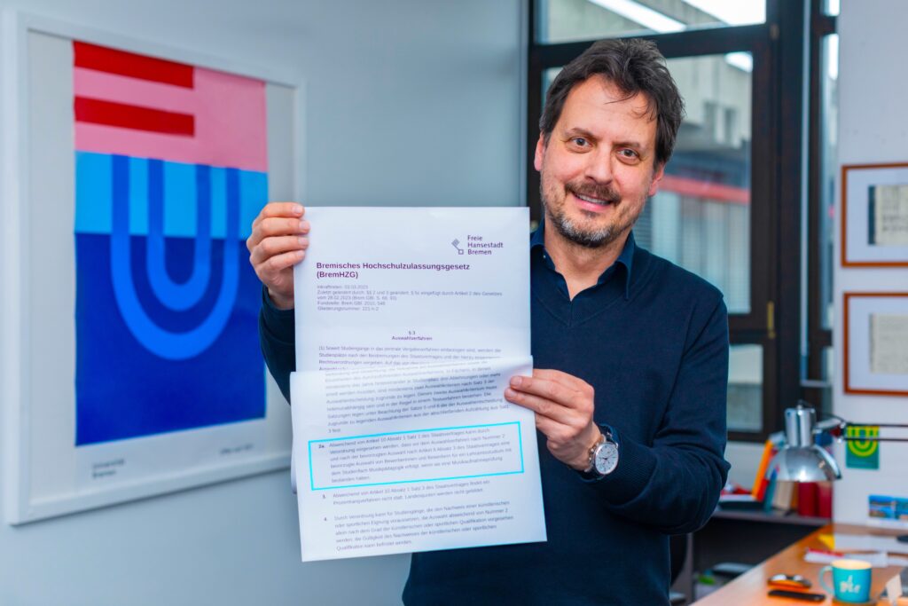 Professor Alexander Cvetko lächelt in die Kamera und hält einen Ausdruck vom Bremischen Hochschulzulassungsgesetz in den Händen