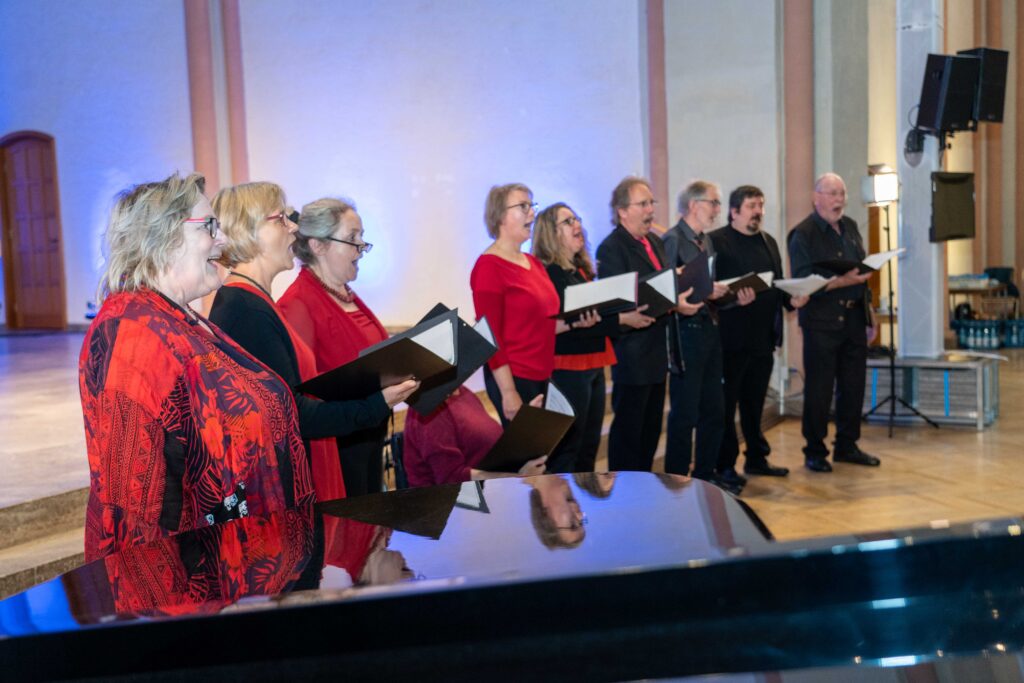 Ein rot und schwarz gekleidetes gemischtes Vokalensemble steht singend in der Kulturkirche St. Stephani