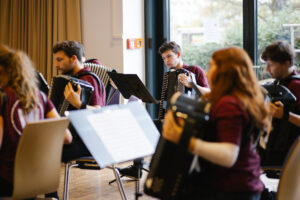 Nahaufnahme von jungen Menschen, die auf ihren Akkordeons spielen und konzentriert in die Noten blicken.