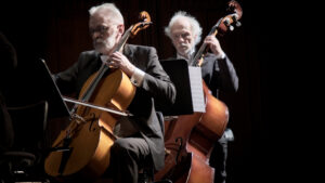 Ein Cellist und ein Kontrabassist, die hintereinander sitzen und während des Spielens konzentriert in ihre Noten blicken.