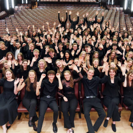 Gruppenfoto bei der Preisverleihung des Würth-Preises. Eine große Gruppe jungen Menschen in schwarzer Kleidung sitzt im Zuschauerraum des Konzertsaals "Die Glocke". Die Jugendlichen schauen glücklich in die Kamera und strecken ihre Hände in die Höhe.