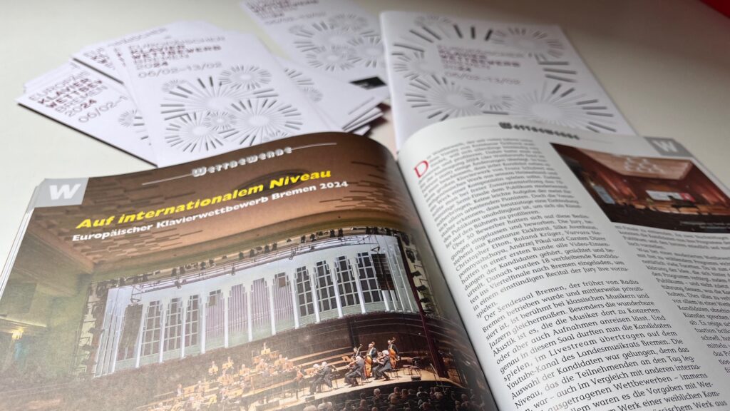 Aufgeschlagene Zeitschrift mit einem Artikel über den Europäischen Klavierwettbewerb Bremen 2024 und einem Foto eines Orchesters in einem Saal mit großen Fenstern